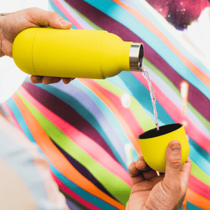 בקבוק תרמי נייד בצבע צהוב במצב פתוח בעת מזיגה לכוס שהיא המכסה